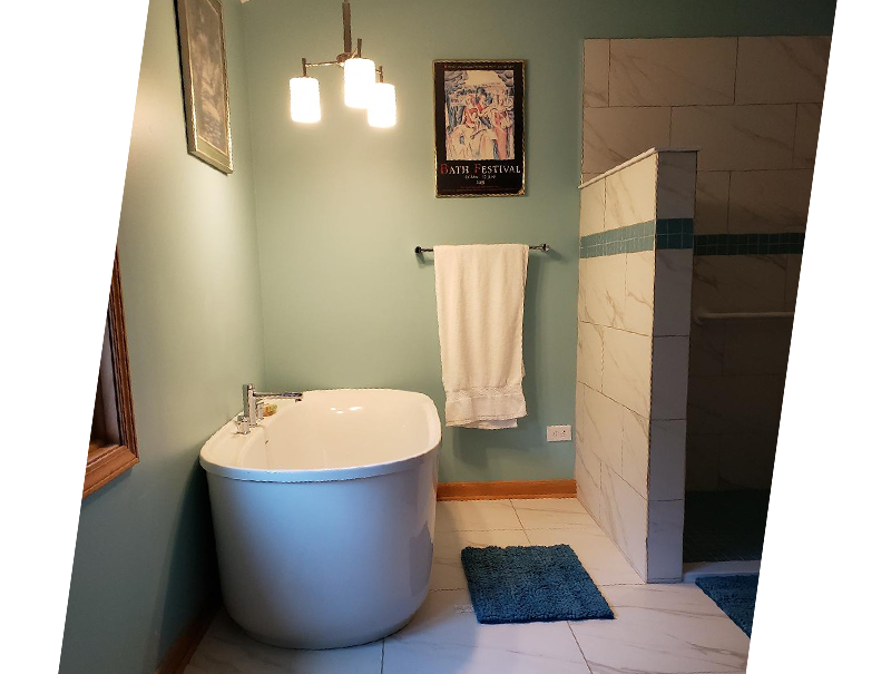 Closeup of freestanding tub with chandelier lit. There's a picture on the wall and bathmat in front of the tub.